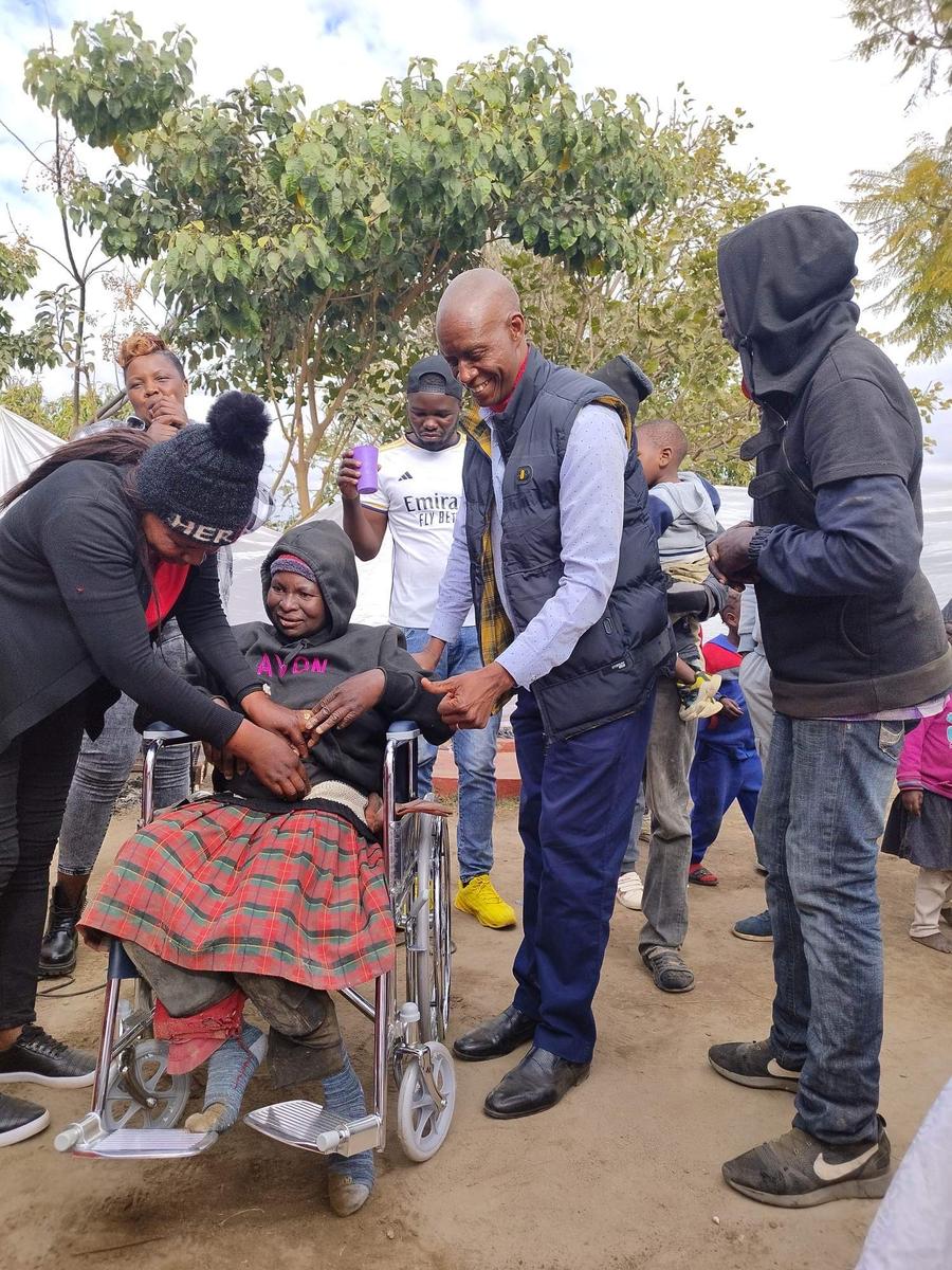 NFM team member presenting a wheelchair to an elderly woman in Zimbabwe, with helpers gathered around