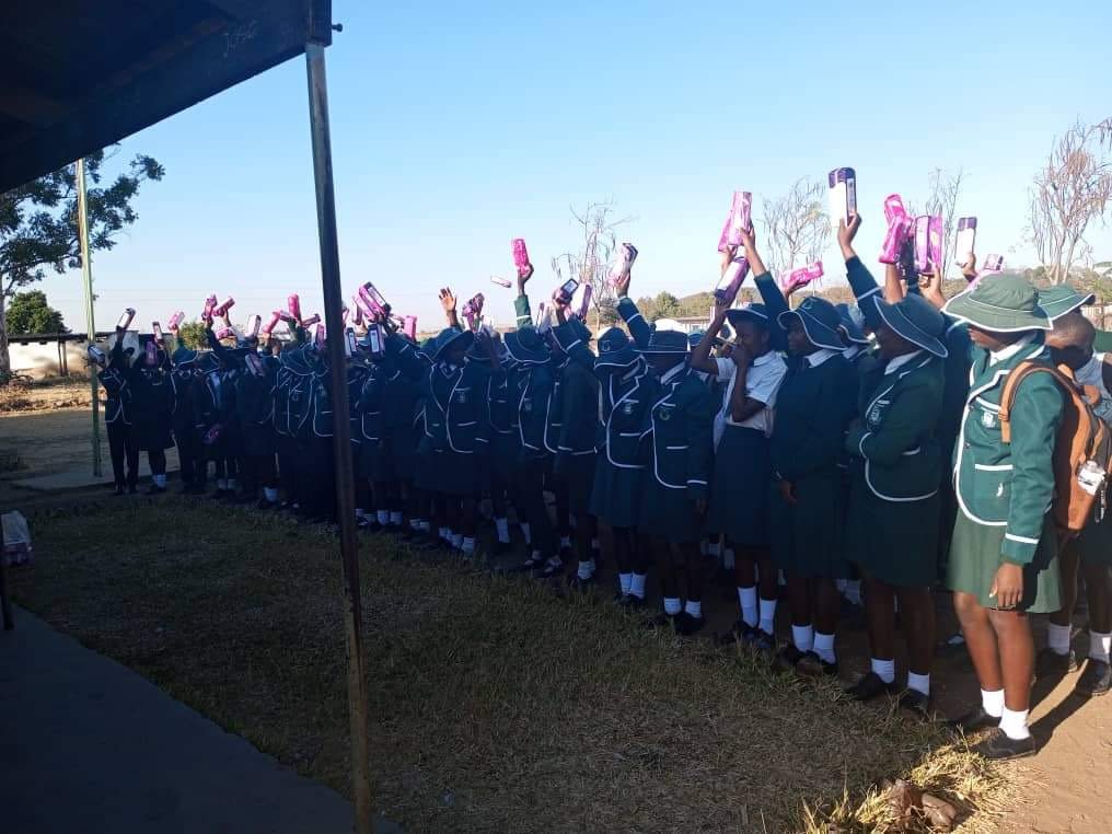 Line of schoolchildren in green uniforms waving gift bags outdoors