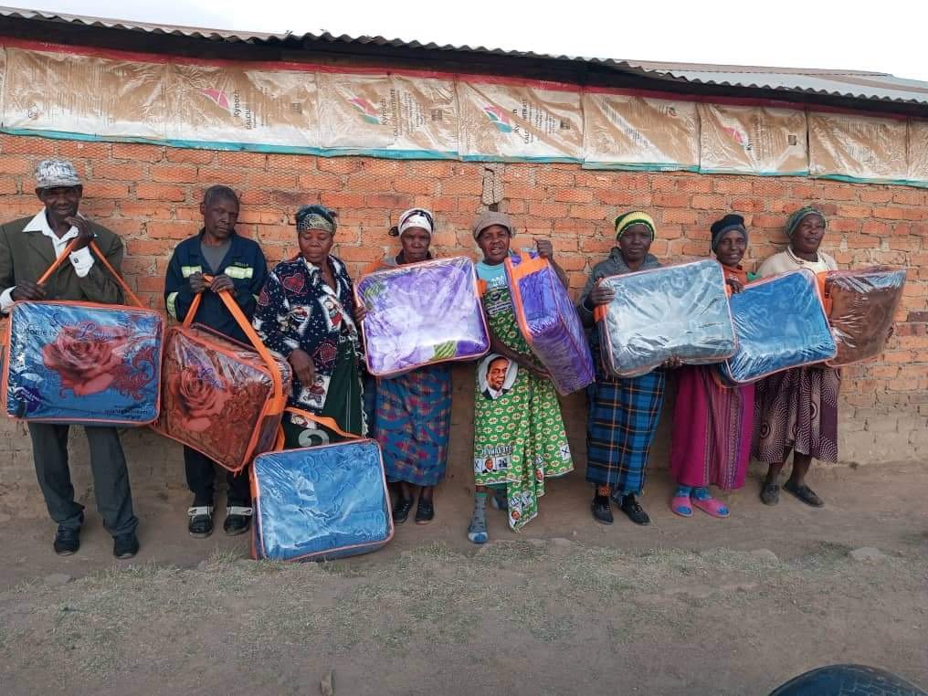 Women and children holding colorful bags and blankets outside a brick building