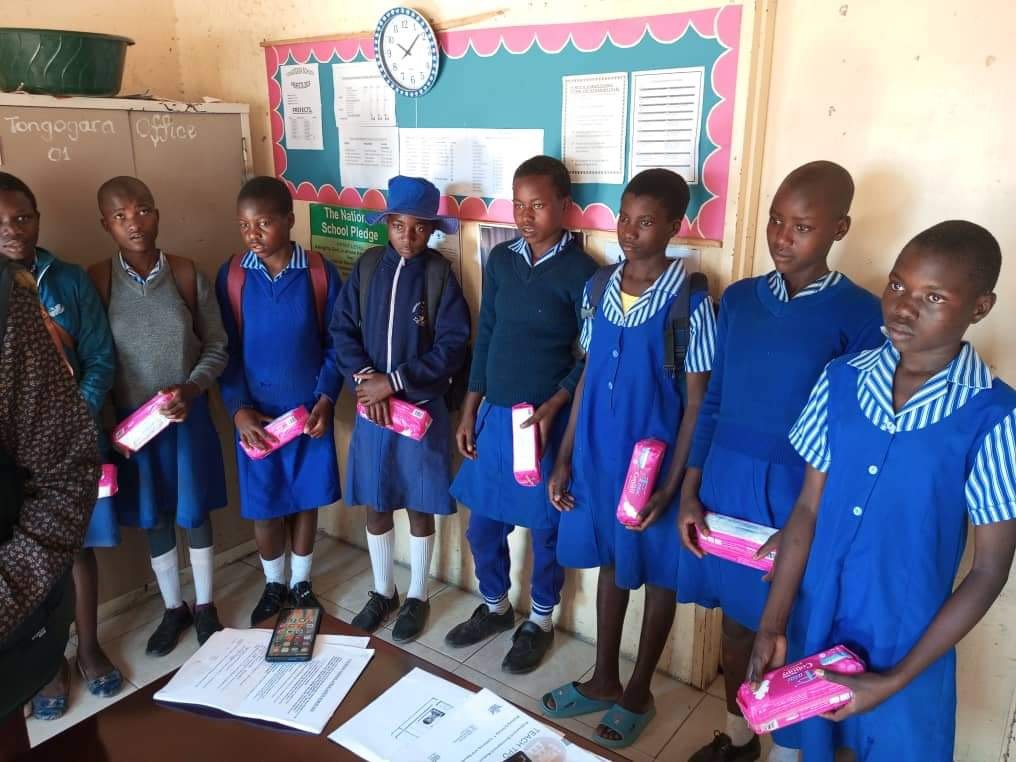 Girls in blue school uniforms holding pink gift bags indoors